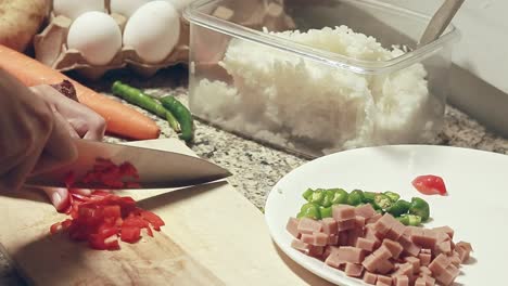 chopping red paprika and setting it aside among diced chili and ham, preparing the ingredients for a fried rice recipe