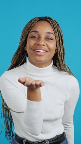 young african american woman blowing a kiss, puckering her lips, and waving on a blue background
