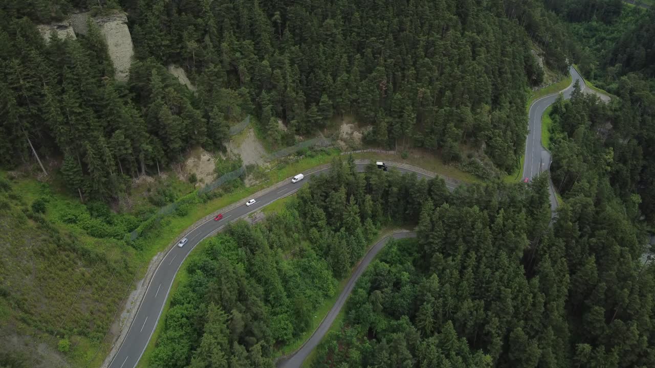 Smooth drone tracking shot above vehicles cruising along a winding mountain road through the lush alpine landscape of Tyrol, Austria
