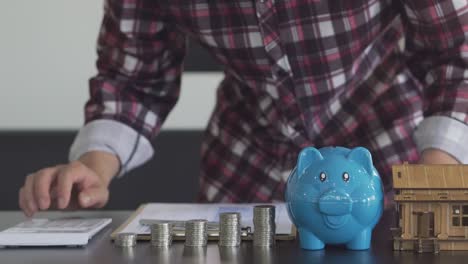 joven contando monedas en una alcancía para ahorrar dinero, comprar una casa, conceptos financieros y económicos. cuentas de gastos mensuales y reembolsos de deudas usando calculadoras y documentos fiscales en casa.