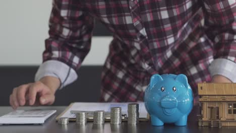 young man counting coins in a piggy bank to save money, buy a house, financial and economic concepts. monthly expenditure accounts and debt repayments using calculators and tax documents at home.