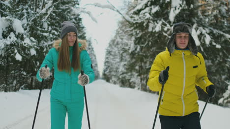 Ein-Mann-In-Einer-Gelben-Jacke-Und-Eine-Frau-In-Einem-Blauen-Overall-Im-Winter-Im-Wald-Beim-Skifahren-In-Zeitlupe