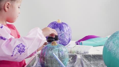 mother and daughter decorating art pumpkins with glitter