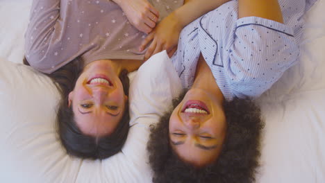 overhead portrait shot of loving same sex female couple wearing pyjamas lying on bed at home