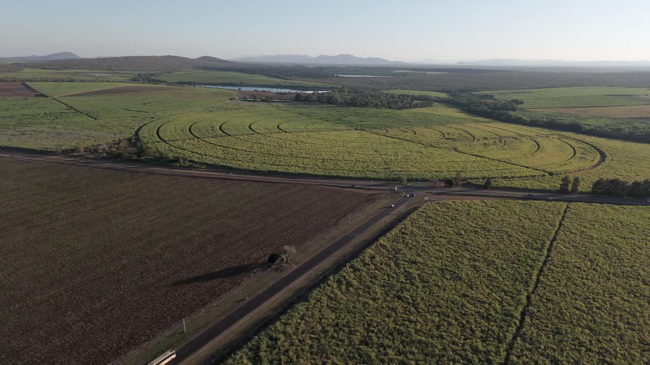 vista de avión no tripulado de las granjas de caña de azúcar y pimienta en una colcha de patchwork, dividida por una carretera principal con vehículos que conducen hacia un cruce en t