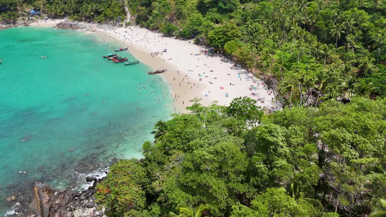 Riprese aeree catturano una spiaggia serena a Phuket, Thailandia, con acque turchesi, vegetazione lussureggiante e visitatori sparsi che si godono il sole