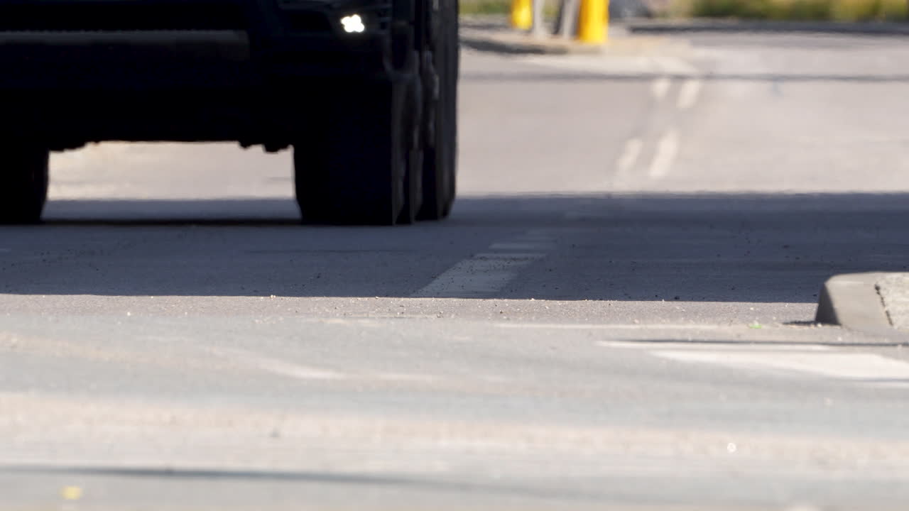 The low angle captures a car's wheel on a concrete road, highlighting the contact point between tire and pavement