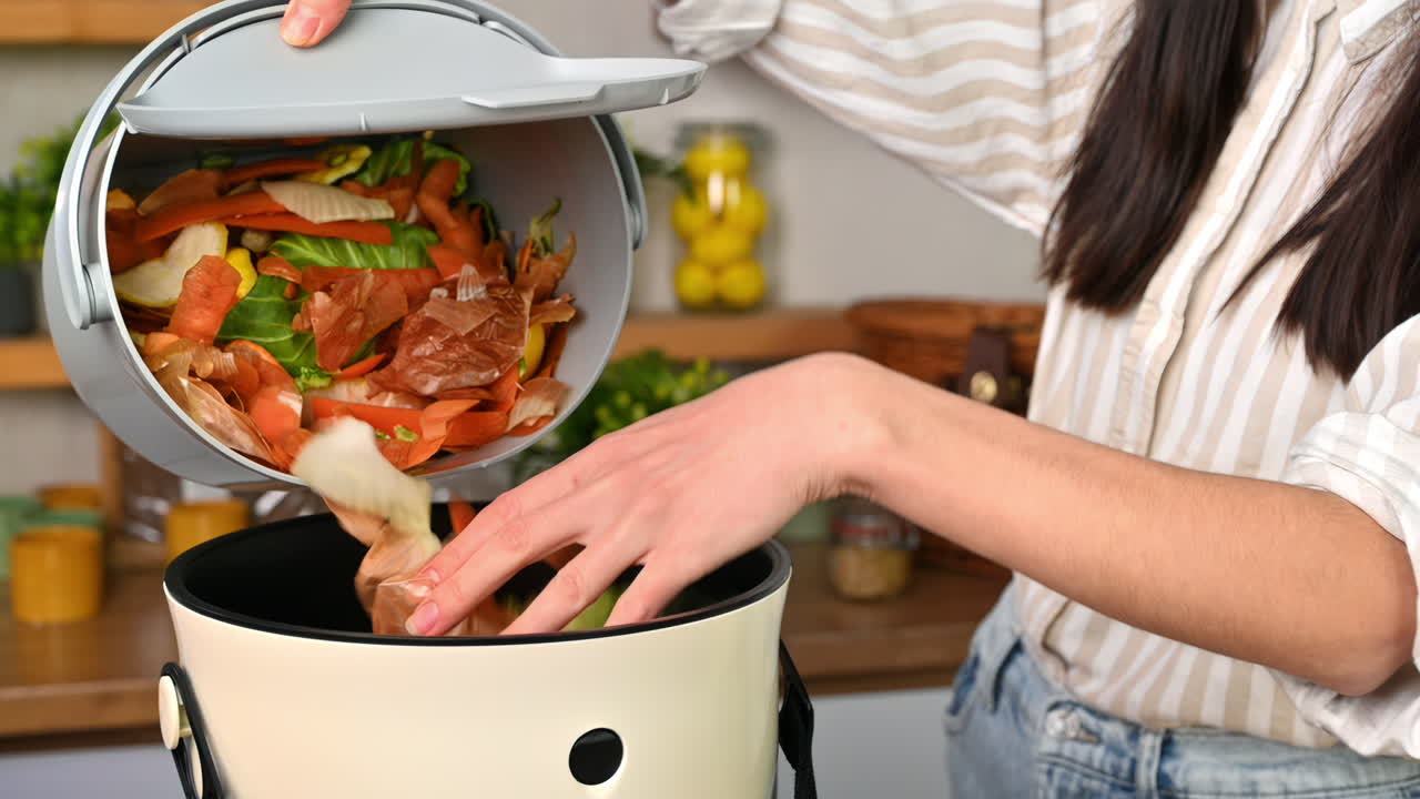 Woman throwing vegetables peels in a compost bin from a collection vessel. Housewife cooking food and composting organic waste in a bokashi container at home. Ecological and sustainability concept