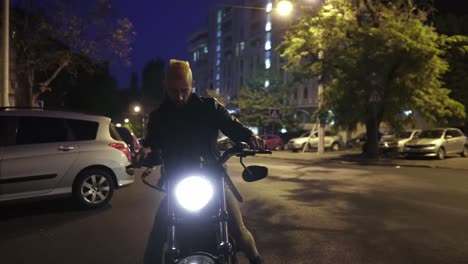 hombre ciclista guapo sentado en una motocicleta de estilo clásico, se enciende desde el estacionamiento por la noche