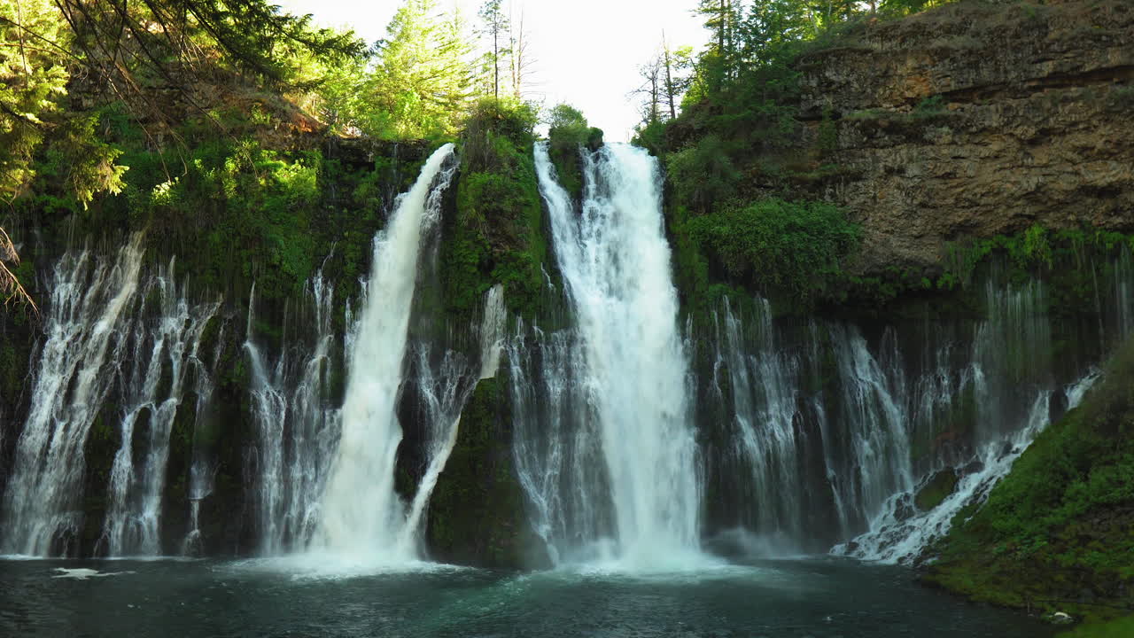 Panorama of Burney Falls, forest waterfall in California, with water falling down a mossy cliff