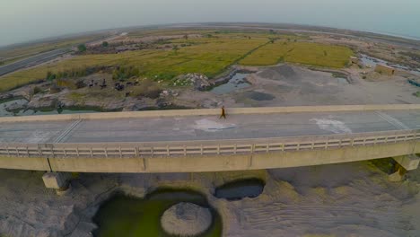 Aerial-view-of-Under-constructed-bridge-over-the-river-with-heavy-duty-trucks-and-machinery,-Farms-and-buffaloes-in-the-river