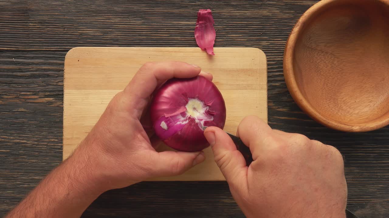 Top view of male hands peeling a red onion on the wooden board