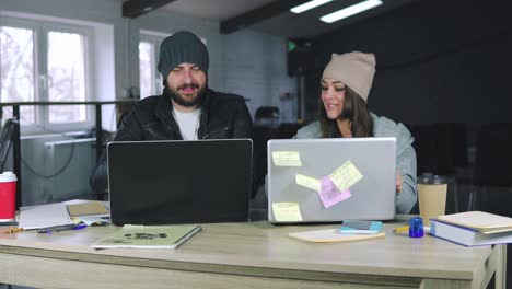 Young-man-and-woman-are-working-together-in-front-of-their-laptops,-sitting-together-at-the-table.-They-celebrate-a-successful