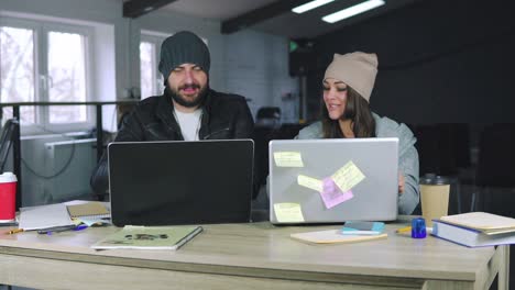 young man and woman are working together in front of their laptops, sitting together at the table. they celebrate a successful