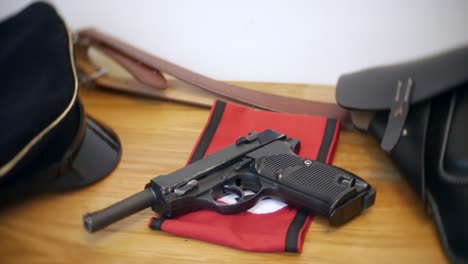 a german second world war p38 pistol, an officer's black visor cap, armband, belt and holster are on a wooden table