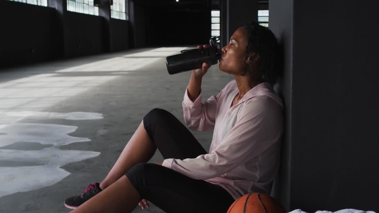 African american woman sitting in an empty building resting drinking water