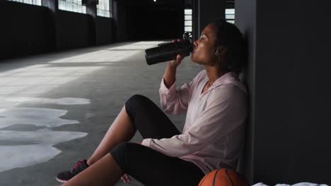 mujer afroamericana sentada en un edificio vacío descansando bebiendo agua