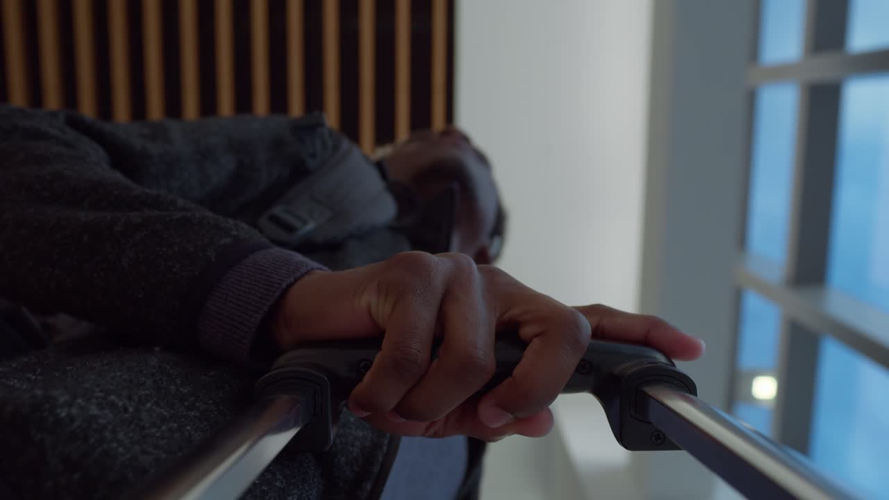 la mano de un viajero masculino agarrando el mango de una maleta rodante y caminando a través de la terminal en un aeropuerto moderno - cámara lenta