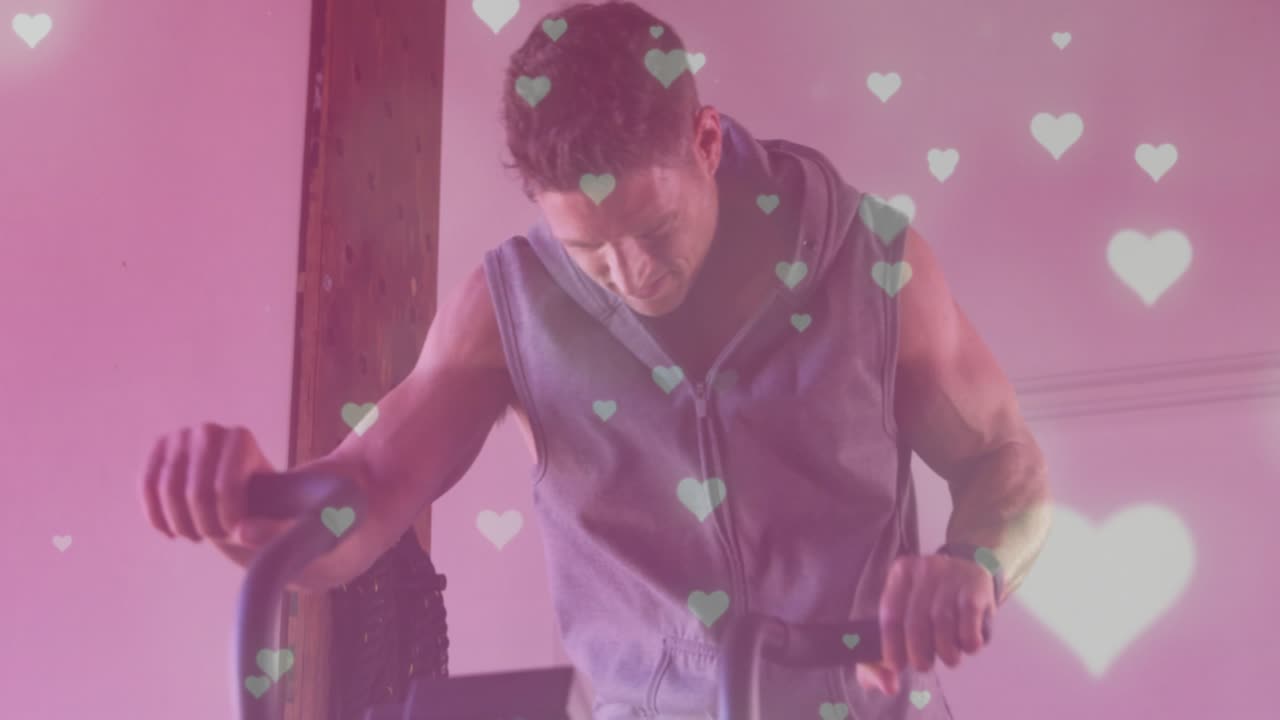 Man tapping elliptical console and pedaling in sunlit loft, heart bokeh on lens, fitness focus