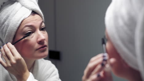 young attractive woman applies mascara while looking in the mirror