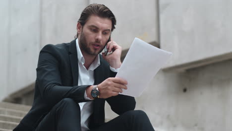 Business-man-calling-on-smartphone-in-city.Male-professional-working-with-papers