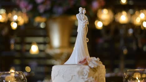 Close-up-on-miniature-bride-and-groom-on-top-of-cake,-dark-defocused-background,-candlelight-only,-romantic-atmosphere