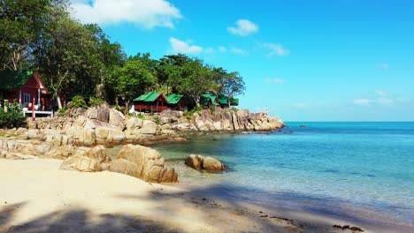 calm exotic beach with sand and cliffs on shore washed by calm turquoise sea, bungalows under trees with ocean view in thailand