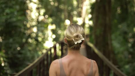 wunderschöne blonde frau, die im tropischen dschungel lächelt, die schönheit der natur genießt, auf einem holzsteg im cahuita-nationalpark spazieren geht