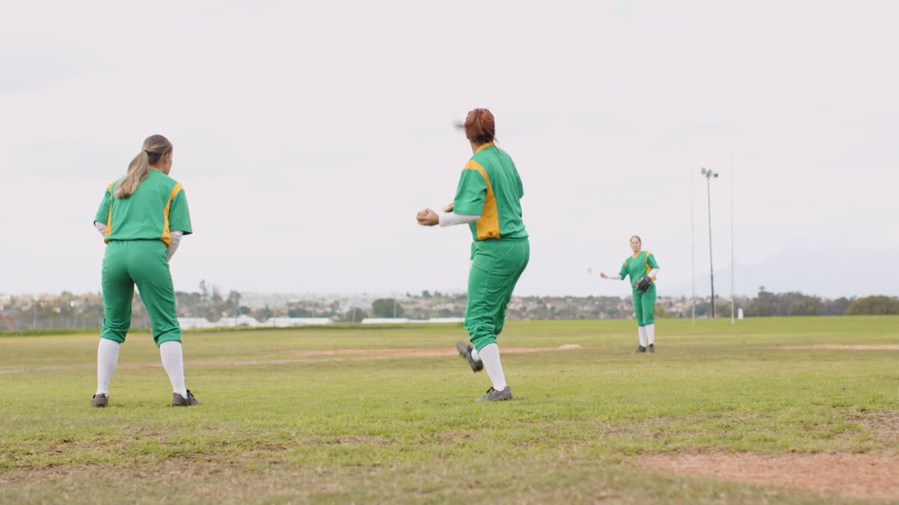 Multiracial female baseball players catching and throwing the ball to each other on a pitch