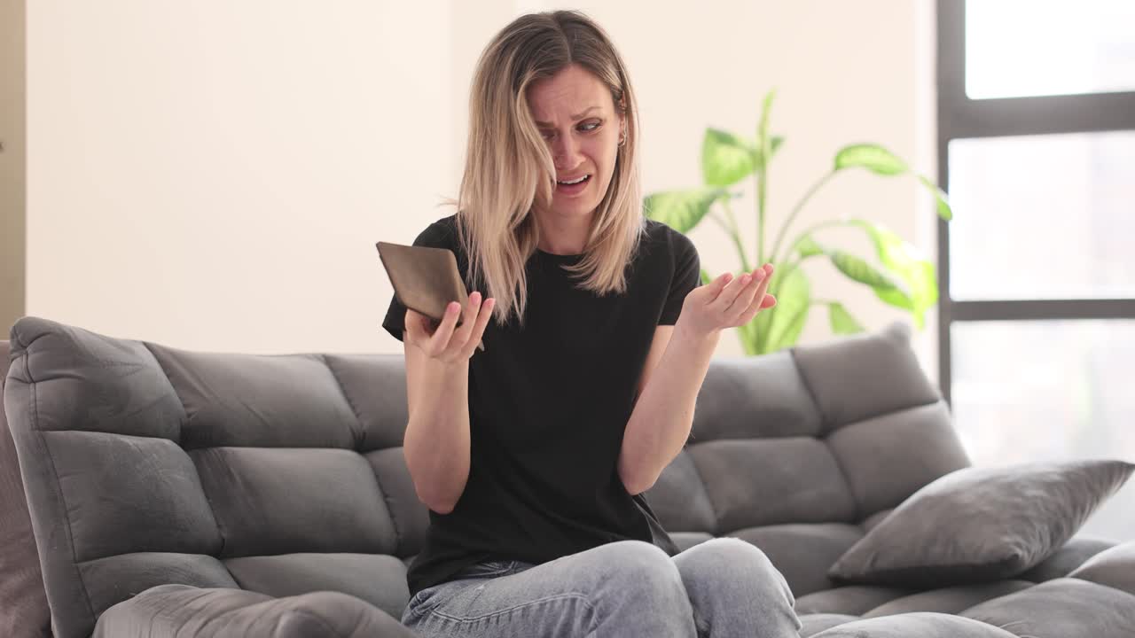 Sad woman with empty wallet on couch