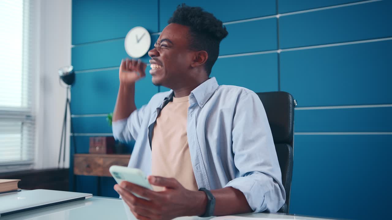 Overjoyed young african american man rejoices positive news in mobile phone