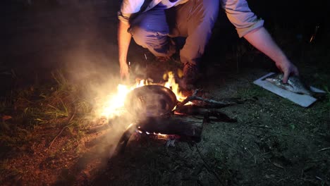 a man cooks a bream on a frying pan over a fire in australia at night