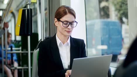 Young-Attractive-Businesswoman-In-Glasses-Going-Home-In-The-Tram-And-Working-On-The-Laptop-Computer-As-Being-Very-Busy