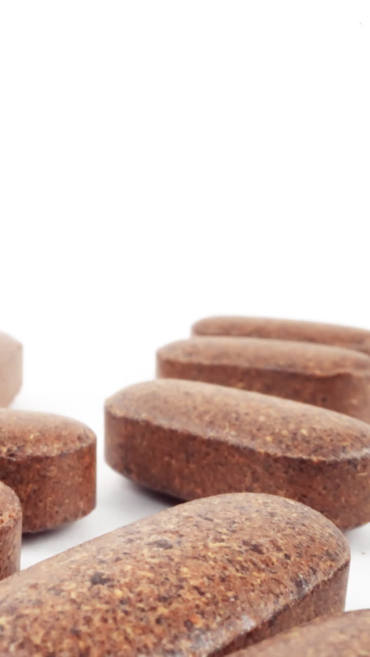 comprimidos de suplementos nutricionales marrones dispuestos artísticamente sobre un fondo blanco puro