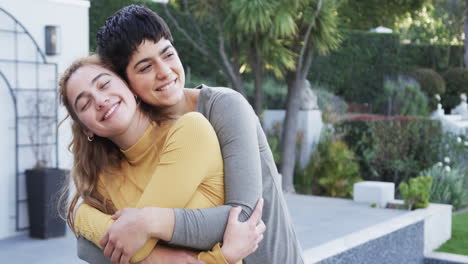 Happy-caucasian-lesbian-couple-standing,-embracing-and-smiling-in-front-of-house