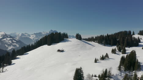 Aerial-of-single,-remote-cabin-in-snow-covered-mountainscape