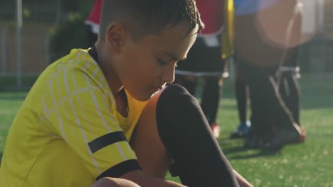 mixed race soccer kid lacing up his shoe in a sunny day