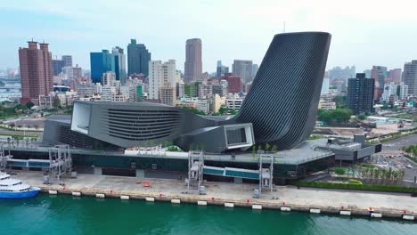 Toma-Panorámica-Aérea-Del-Edificio-Moderno-En-La-Terminal-Portuaria-Y-El-Horizonte-De-Kaohsiung-En-El-Fondo,-Taiwán