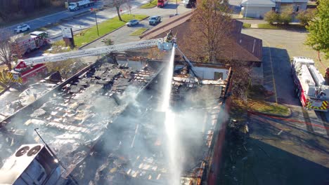 two hoses simultaneously putting out smoking roof of large building, wide aerial