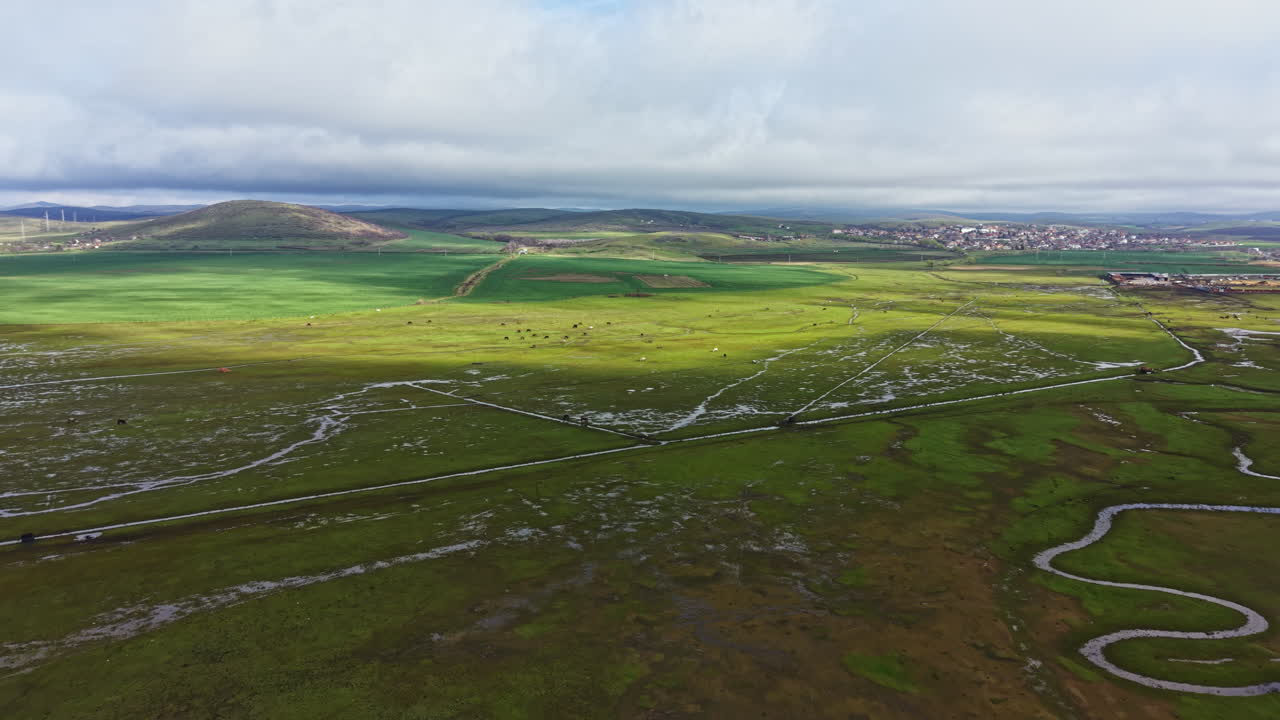 Grønt landskab med snoet flod under overskyet himmel i landområde om dagen