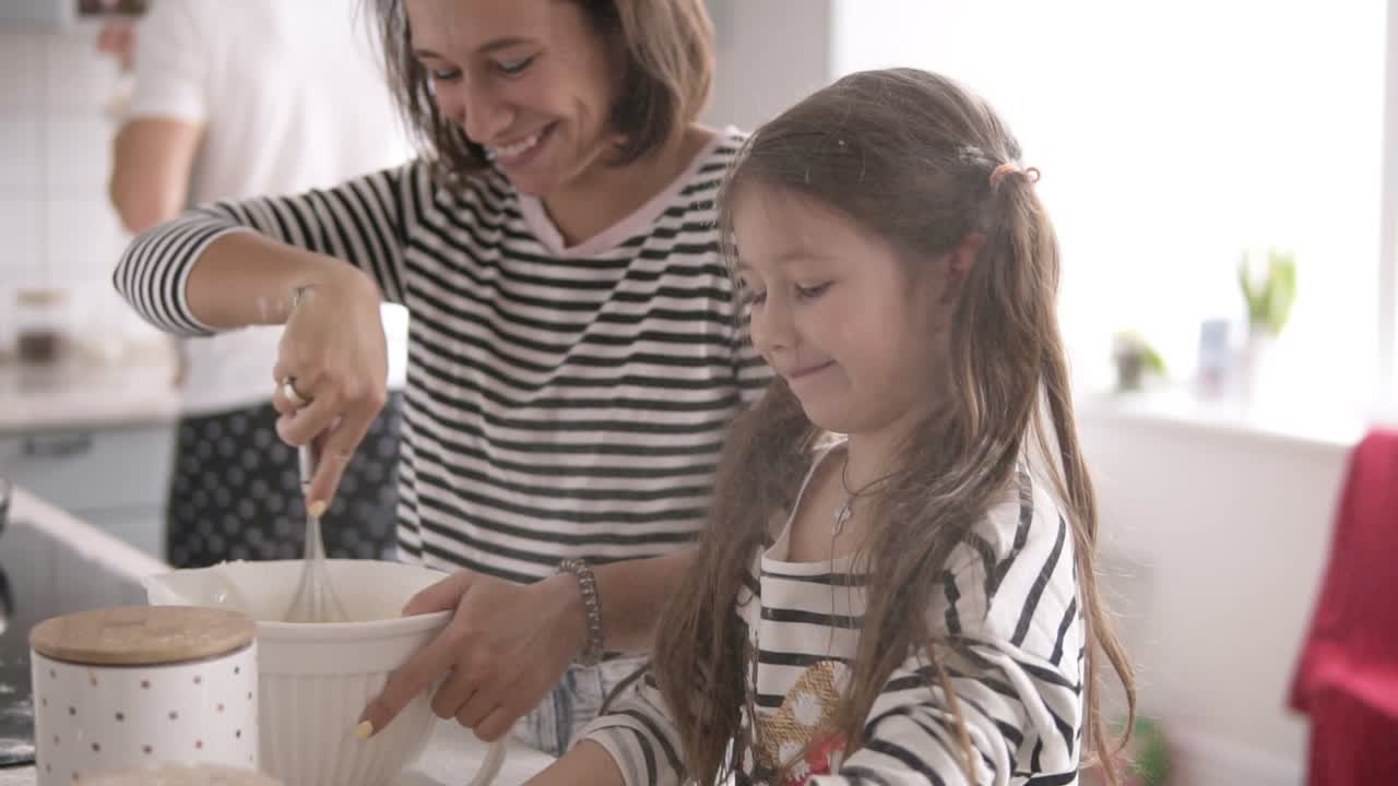 la hija lanza harina y la madre está amasando la masa en la cocina