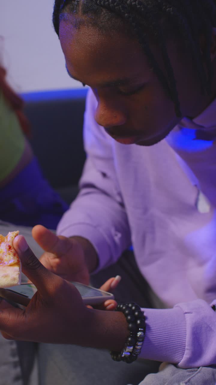 Vertical Video Of Group Of Gen Z Friends Sitting On Sofa At Home Gaming And Eating Takeaway Pizza