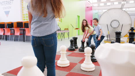 tres niños jugando al ajedrez gigante en un centro de actividades científicas