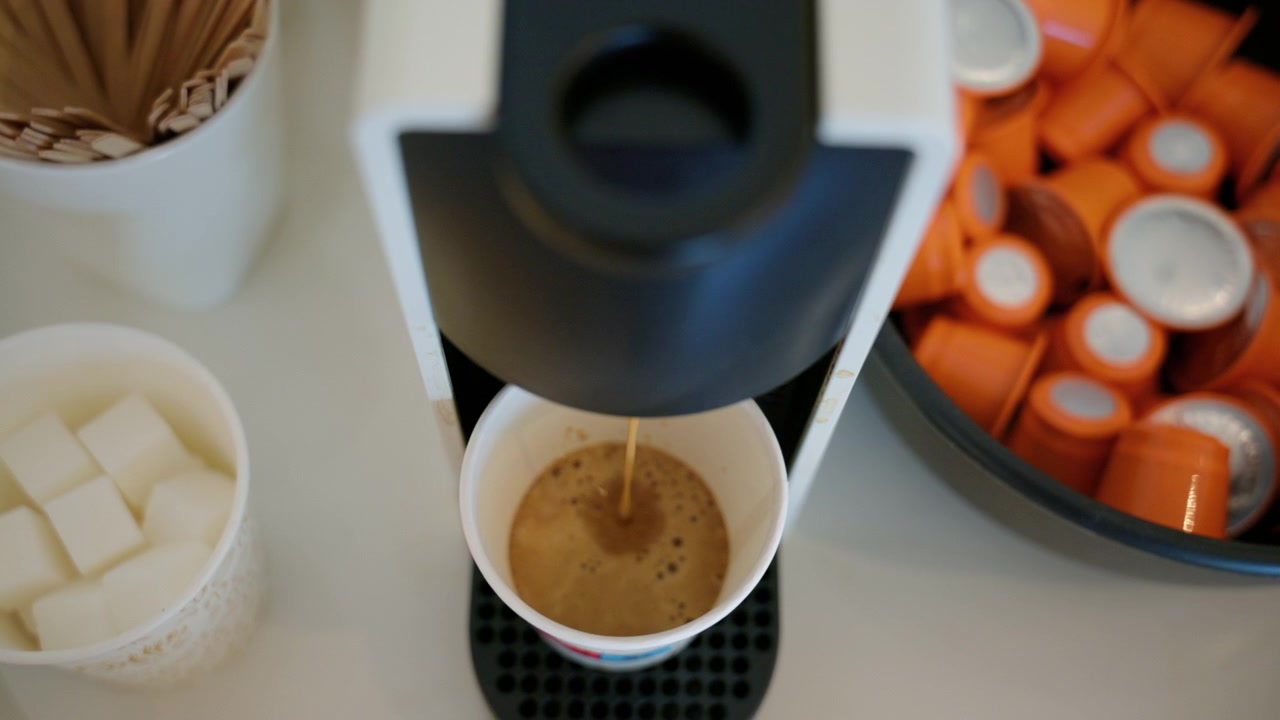 Coffee machine preparing a hot espresso in a disposable cup, with sugar cubes and coffee capsules nearby. Perfect for a quick break
