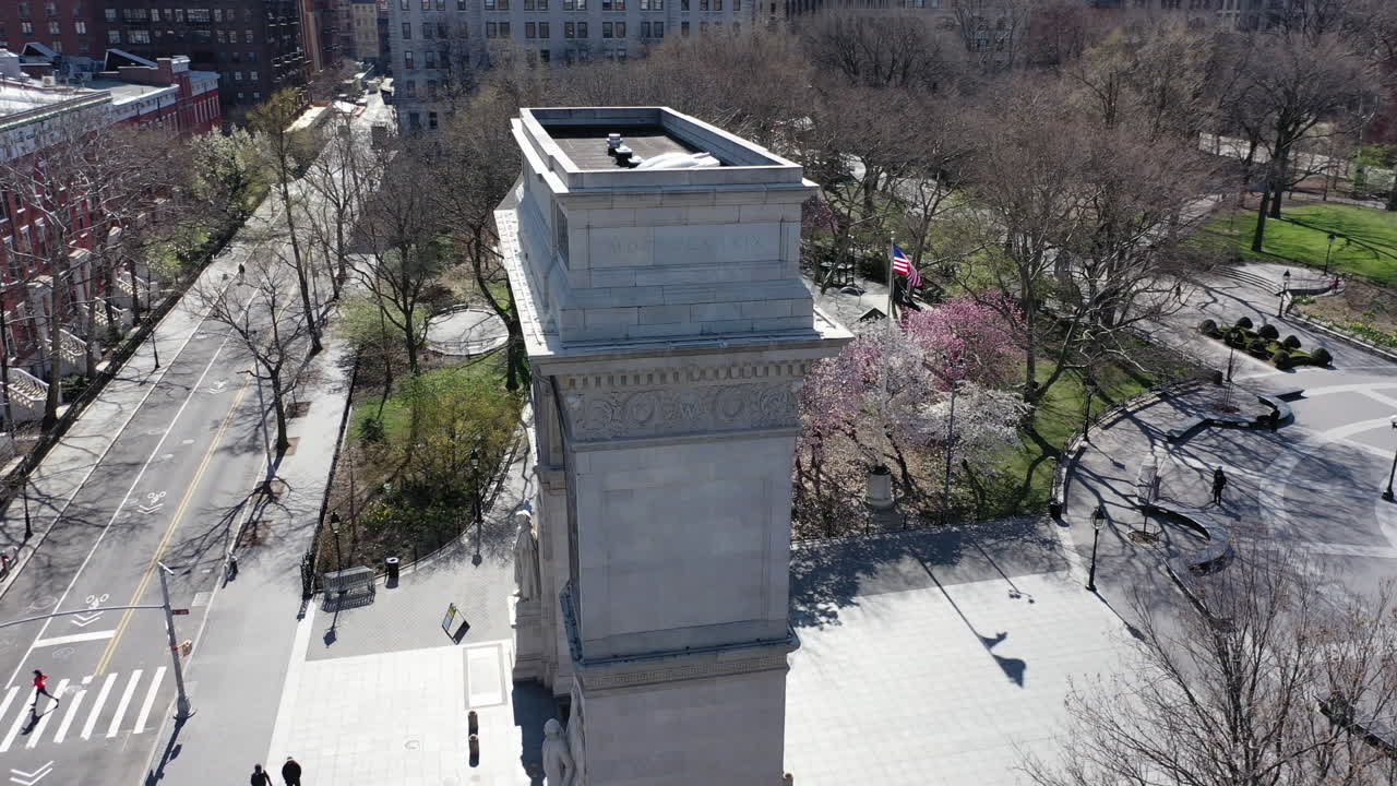 A low aerial, day time view of the Washington Square Arch. The drone orbits the arch, counterclockwise with the very empty Washington Square Park in the background.