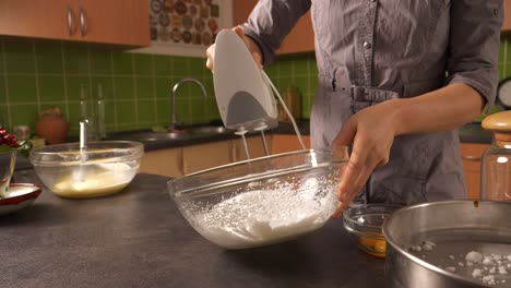 un primer plano de una mujer joven usando una batidora eléctrica mezclando azúcar de vainilla, sal y claras de huevo para crear espuma para un relleno de pastel