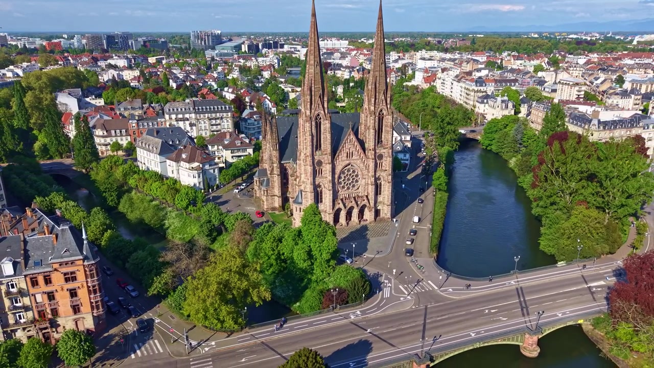 Fransa, Strasbourg'da nehir kenarındaki Saint Paul Kilisesi, arka planda modern Avrupa Parlamentosu binasıyla. Havadan drone geri çekimi