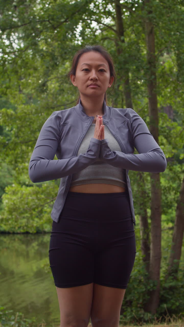 video vertical de una mujer con ropa deportiva haciendo yoga se estira en una alfombra en el bosque junto a un lago o río disfrutando de la paz y la belleza de la naturaleza filmado en tiempo real 1