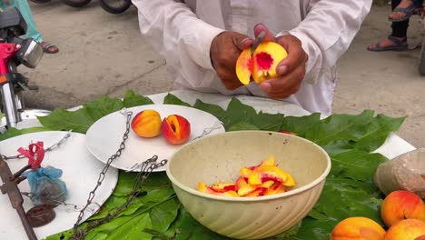 a local fruit seller skillfully slices fresh peaches into a bowl at a roadside stand in pakistan.