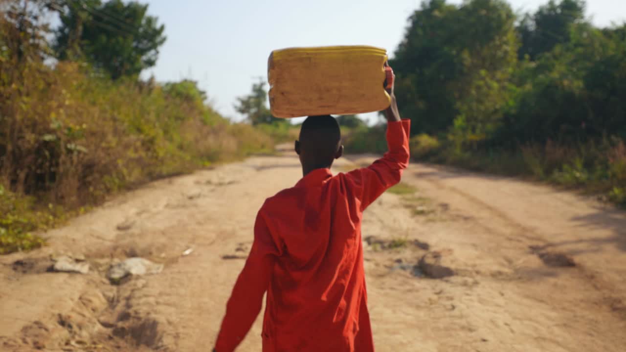 African kid carrying water bottle on his head after fetching water from the river